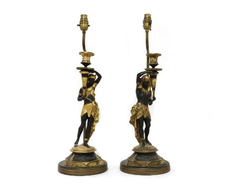A pair of Egyptian Revival figurative parcel-gilt candlestick lamps,each painted composition subject, holding a torchère scon