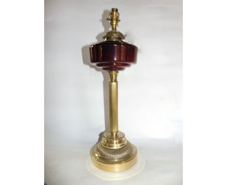 An electrified brass oil lamp raised on a fluted column and stepped circular base with a ruby glass reservoir 47 cm tall appr