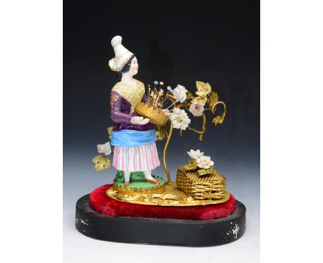 A 19th century continental figure of a girl in traditional costume supporting a gilt metal and velvet pin cushion set with co