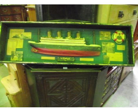 A wall mounted display case containing a half hull model of the Titanic flanked by emphemera together with an early 20th cent