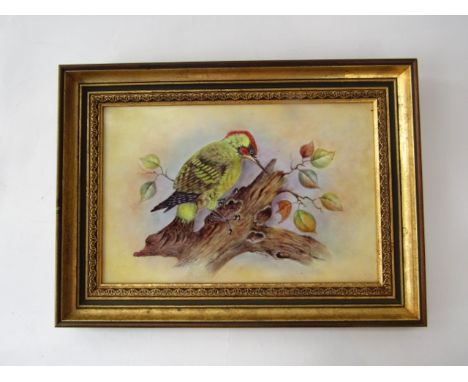 A rectangular ceramic plaque with painted decoration of a green woodpecker on a branch, signed G Delaney, with printed mark t