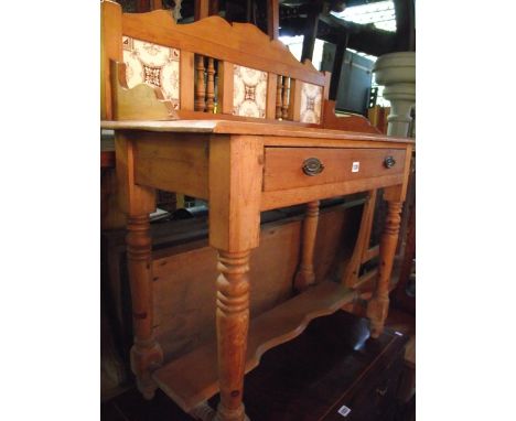 A late Victorian stripped pine washstand, the raised back incorporating three transfer printed ceramic tiles over a shallow f