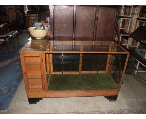 A vintage oak floor standing shop display counter, with plate glass panels incorporating a small sectional cupboard and till,