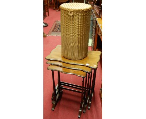 A shaped mahogany nest of three occasional tables; together with a Lloyd Loom wicker circular laundry basket, with hinged cov