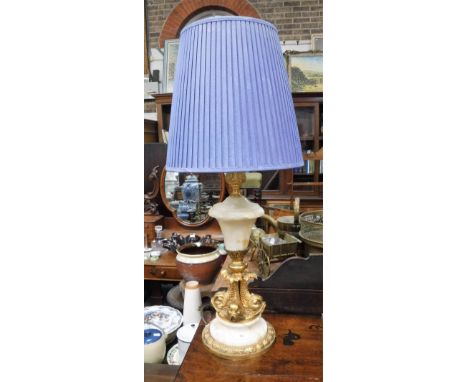 A GILT METAL AND WHITE ALABASTER TABLE LAMP, the base decorated with stylised dolphins, fitted a blue pleated shade, 31.5" hi