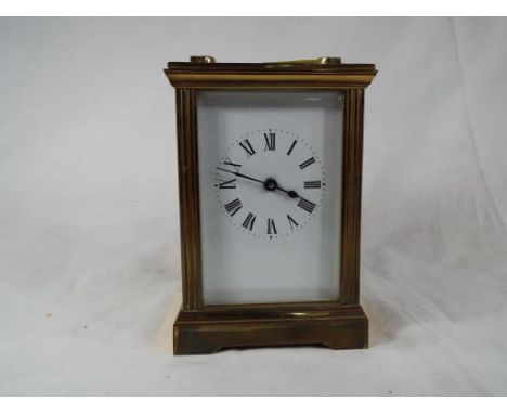 A brass cased carriage style timepiece with glazed bevelled panels, opening rear door, white enamel dial with Roman numerals,
