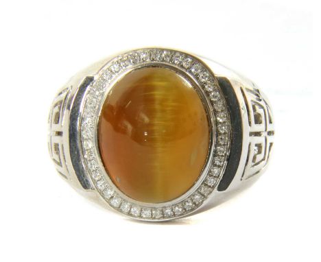 A white gold tiger's eye and diamond ring, an oval cabochon tiger's eye, rub set to a border of single cut diamonds, grain se