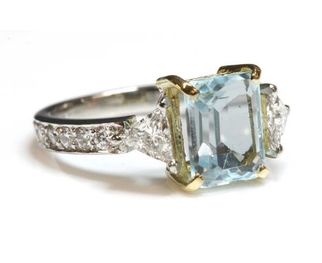 A platinum blue topaz and diamond ring, an emerald cut blue topaz, claw set in a yellow collet, with a triangular cut diamond