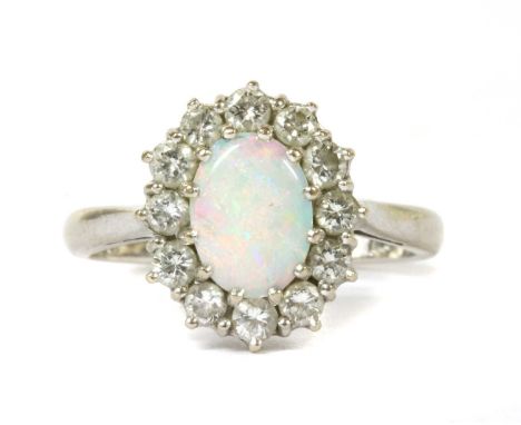 A white gold opal and diamond cluster ring, an oval cabochon opal and surround of brilliant cut diamonds, claw set to a wire 