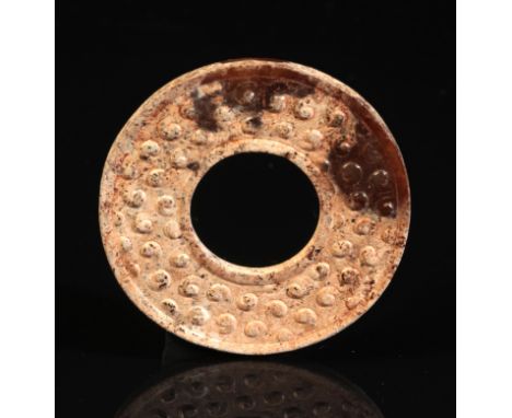 A CHINESE JADE 'GRAIN PATTERN' DISC probably Han dynasty, with moulded edges and a dense pattern of bosses raised in relief, 
