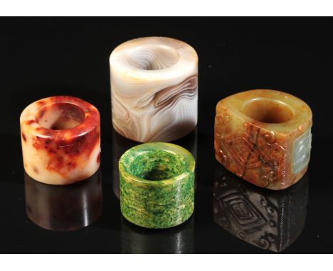 A GROUP OF FOUR CHINESE ARCHER'S RINGS including an agate example, 3.5cm high, and another in carved jade, 3cm high (4)