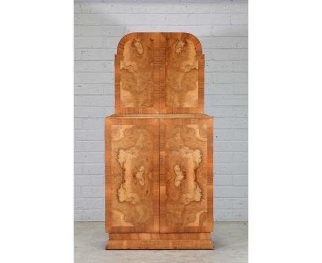 An Art Deco walnut and crossbanded cocktail cabinet, the arched upper section opening to reveal a mirrored interior with two 