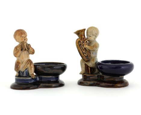 Two Doulton stoneware figural salts, by George Tinworth, one modelled as a putto playing cymbals, the other a putto playing a