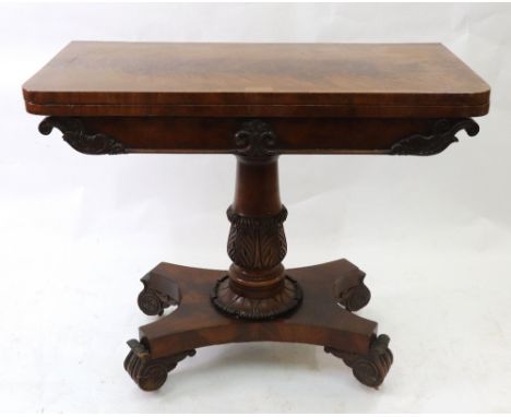 A William IV mahogany card table, the hinged fold over top above a scroll carved frieze, on a turned and lotus carved pillar 