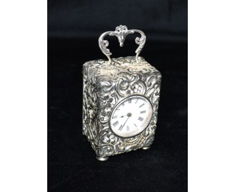 A SILVER CARRIAGE CLOCK  The case with heavily embossed scroll fancy pattern, scroll handle and four shallow pad feet the clo