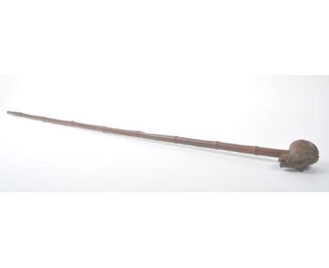 A Burmese bamboo wood carved opium pipe with brass mouthpiece and carved robed figure to the underside of the bowl. Measuring