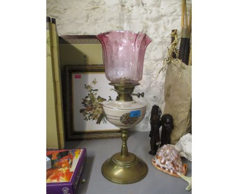 A Victorian oil lamp with a cranberry shade, beige and floral reservoir, on a brass stand