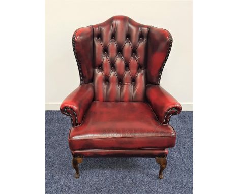 CHESTERFIELD SHAPED WINGBACK ARMCHAIRin ox blood red leather with a button back and scroll arms with decorative stud detail, 