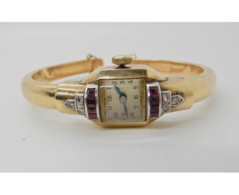 A YELLOW METAL ART DECO STYLE BANGLE WATCH set with diamonds and red gems, Swiss movement, 16 jewels, inner diameter 4.8cm x 