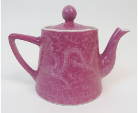 A CHINESE PORCELAIN TEAPOT AND COVER incised on a pink ground with two dragons chasing The Flaming Pearl, red four character 