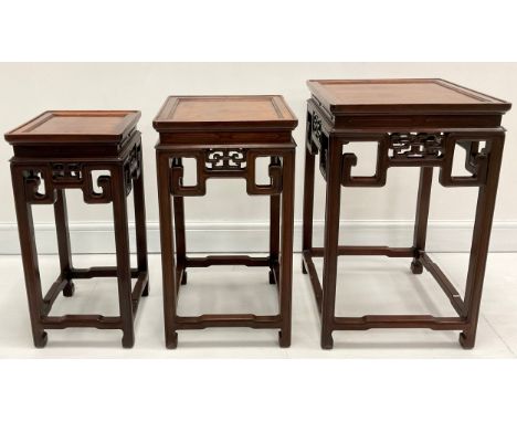 A Chinese stacking nest of three huanghuali occasional tables, panel tops, pierced scroll friezes, the largest 68cm high, 42c