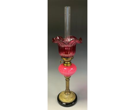 A Victorian style brass and cranberry glass oil lamp of small proportions, shaped shade. milk cranberry globular reservoir, b