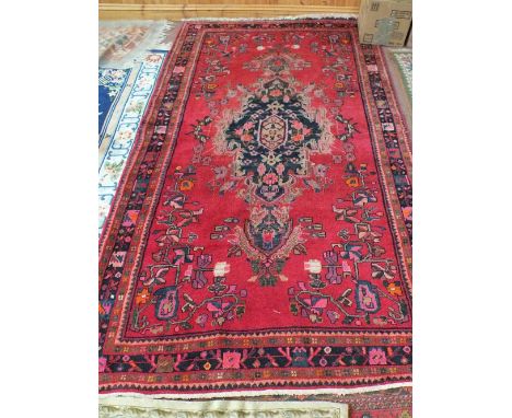 A Persian red ground carpet with stylised floral decoration and central medallion, 120" x 60"