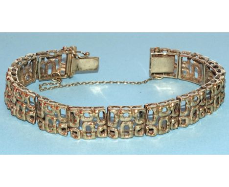 A 9ct gold bracelet c1970's of thirteen pierced and textured plaques of abstract design, with concealed clasp, safety chain a