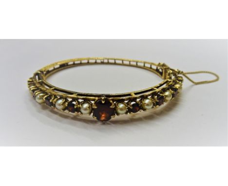 A 9ct gold, garnet and cultured pearl oval hinged bangle, claw set with the principal oval cut garnet, between alternating ci