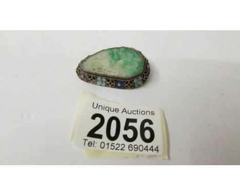 A carved jade brooch with enamelled coloured flowers to edges.