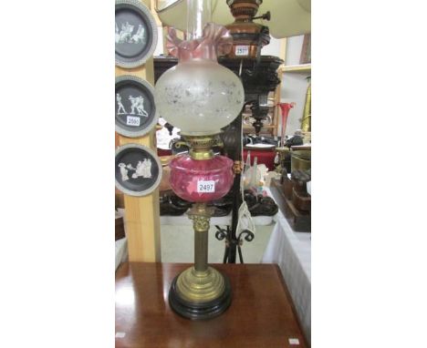 A Victorian brass Corinthian column oil lamp with cranberry glass font and alter shade,