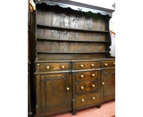 A GEORGE III CONWY VALLEY OAK BREAKFRONT DRESSER, a three shelf shaped belly rack with decorative top apron over a two plank 