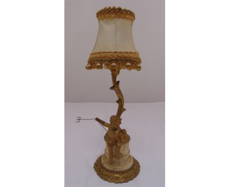 A gilded metal lamp stand in the form of a putti beneath a tree on raised circular plinth,  A/F to include shade, 45cm (h)