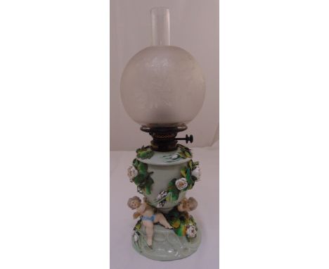 A continental oil lamp the porcelain base decorated with putti and applied flowers, to include glass shade and funnel, 56cm (