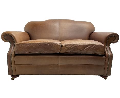 Traditional shape two-seat sofa, shaped back and rolled arms upholstered in tan leather with stud work bands, on compressed b