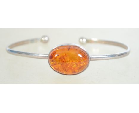 A sterling silver and amber bangle bracelet having a large central amber cabohon with ball finial ends Marked 925 and weighs 