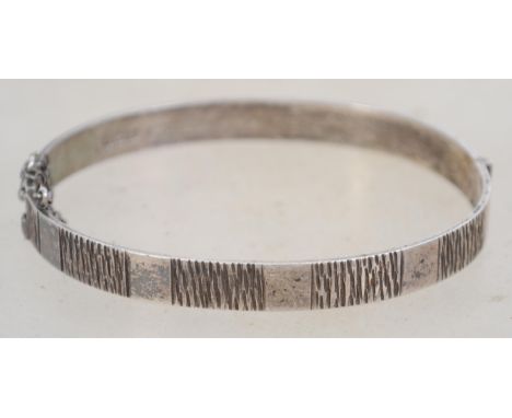A sterling silver bangle bracelet of naturalistic / Brutalist form having a bark effect decoration, hidden clasp and safety c