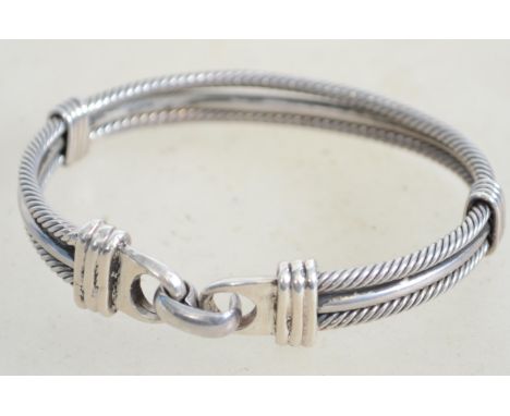 A sterling silver bangle bracelet having two rigid rope twist strands and a central plain strand running through the middle a