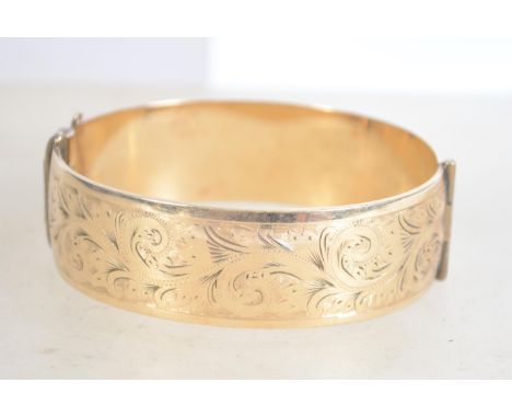 A heavy vintage 9ct rolled gold bangle being half engraved with a foliate design with a box clasp. Marked 9ct gold metalcore.