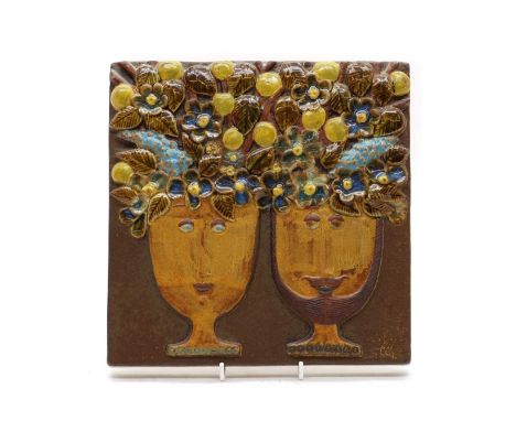 A Gustavsberg glazed wall plaque,Stig Lindberg, depicting two heads on cups, with fruit and leaves, in raised profiles, print