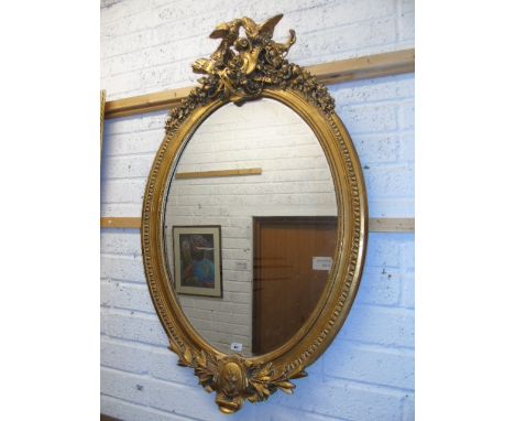 A Continental Highly Moulded Gilt Wall Mirror, the top surmounted by a pair of eagles, the oval glass with beaded surround. €