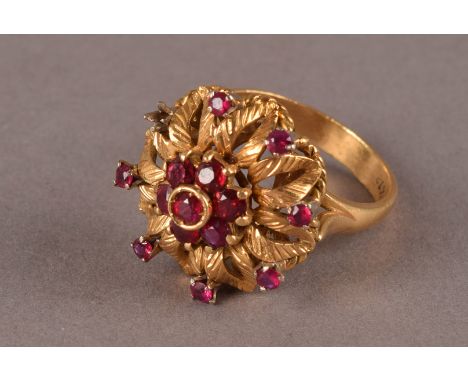 An 18k marked gold ruby ring, the tall top with small ruby style cluster section, surrounded by pierced and engraved section 