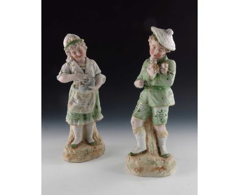 A pair of Gebruder Heubach bisque figures of children, both in green costumes highlighted in gilt, modelled holding puppies a