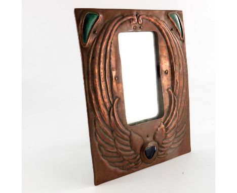 An Arts and Crafts copper and cabochon set mirror, repousse embossed with wings flanking a ceramic heart, the top corners wit