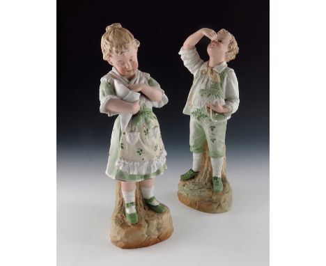A pair of Gebruder Heubach bisque figures of children, both in green foliate painted costumes highlighted in gilt, modelled e
