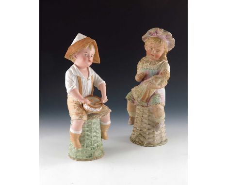 A pair of Gebruder Heubach bisque figures of children, modelled sitting on upturned wicker baskets, the girl holding a doll, 