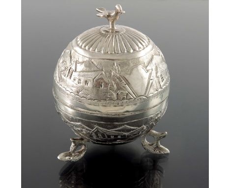 An Oriental silver spherical box, repousse embossed with bands of mountain village scenes, on three cast dolphin feet, surmou