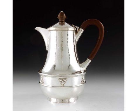 A E Jones, an Arts and Crafts silver jug, Birmingham 1935, planished baluster form, cast with a band of triangular foliate mo