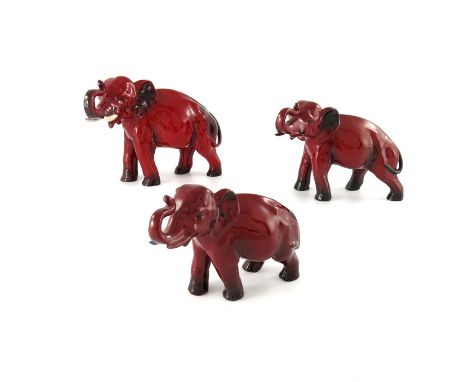 Charles Noke for Royal Doulton, a graduated set of three Flambe Elephant figures, modelled with trunk raised, the largest wit