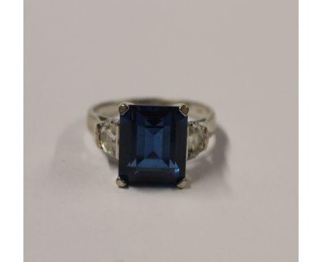 A 14ct white gold ladies' dress ring with emerald-cut blue/green stone (tests as amethyst) and single white stone to each sho